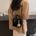 Chic black crossbody bucket bag with plush monster charm on trendy earth tone outfit - Black