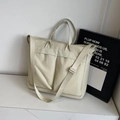 Creamy beige nylon tote bag with dual front pockets and adjustable strap shown on marble - Off-white