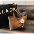 Detalle de un bolso tote de cuero marrón con colgante de monstruo de peluche en sofá - Caqui con Colgante