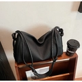 Detailed close-up of a black pleated leather tote bag with a rope strap on wood stairs - Black