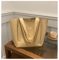 Detail view of large beige faux leather tote bag with front pocket on a coffee table - Khaki