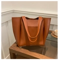 Detail view of a large caramel leather tote bag on a coffee table in a minimalist room - Brown