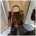 Details einer braunen Bucket-Bag mit goldener Hardware und gestreiftem Quasten-Anhänger - Kaffee Mit Dekorativem Anhänger