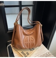 Detailed close-up of a caramel leather tote bag with circular embossed logo on stone surface - Brown