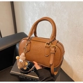 Close-up of brown Boston bag with ATN logo and cute plush charm on a leather chair - With Charm / Brown