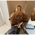 Close-up of deep brown leather Boston bag with PAN TOR logo and gold bell charm detail - With Pendant / Brown