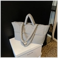 Detailed close-up of a grey quilted down tote bag showing padded nylon fabric on a stand - Gray