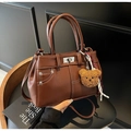 Close-up of brown faux leather handbag with contrast stitching and teddy bear charm - With Charm / Caramel Brown
