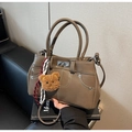 Close-up of brown faux leather handbag with white stitching and bear charm on books - With Charm / Khaki