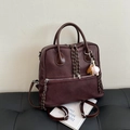 Dark brown faux leather backpack with baseball charm on a black leather bench - Ankora Red With Charms
