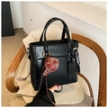 Detail of black oil-wax leather tote bag with a small red checkered hat charm on a chair - Black with Pendant