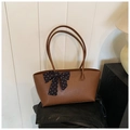 Primer plano de bolso tote de cuero marrón con un lazo decorativo de lunares blancos y negros - Marrón