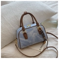Vista dettagliata di una borsa bowling in denim azzurro con manici in pelle marrone e dettagli oro - Marrone con ciondolo