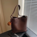 Dunkelbraune Leder-Beuteltasche mit Plüschbär-Anhänger auf schwarzem Buch - Kaffee mit Anhänger