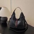 Bolso hobo vintage negro con remaches plateados y borla trenzada sobre un escritorio - Negro