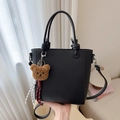 Black pebbled leather crossbody bucket bag with dual handles and a plush bear charm - Black