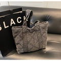 Detalle macro del bolso tote de mezclilla acolchado con costuras de rombos y asas anchas - Negro