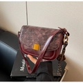 Detail of burgundy crocodile-embossed leather flap and gold metal clasp on saddle bag - With Charm / Burgundy