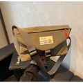 Detail der khakifarbene Kuriertasche mit weißem Logo-Patch und orangem Reißverschluss - Grün