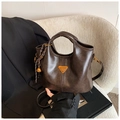 Makroaufnahme einer dunkelbraunen Handtasche mit goldenem Logo und Glocke auf Sofa - Mit Anhänger / Kaffeebraun