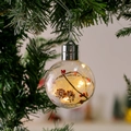 Detail einer klaren Weihnachtskugel mit Tannenzapfen und warmem LED-Licht am Baum - Tannenzapfen-Stil