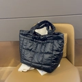Black quilted tote bag with pleated handles and puffy design on a brown leather chair - Black