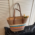 Bolso de paja con rayas tejidas de colores y asas de cuero marrón en ambiente acogedor - Caqui