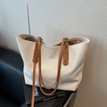 Chic cream woven tote bag with brown leather straps displayed on a vintage book - White
