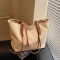 Minimalist beige woven tote bag with brown leather handles on a black leather surface - Light Khaki