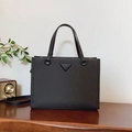 Black tote bag with triangular logo and leather straps placed on a wooden surface - Black