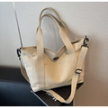Detalle de bolso tote de lona con correa ajustable y bolsillo frontal en fondo texturizado - Beige