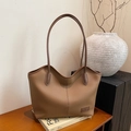 Braune Shopper-Tasche aus Leder mit Litschi-Muster und schmalen Riemen auf Holztisch - Braun