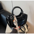 Detail of a black glossy crescent bucket bag with a round handle and colorful charm tag - With Charm / Black