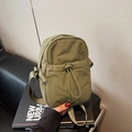 Army green nylon crossbody bag with drawstring pocket on a black decorative book - Green