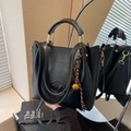 Black bucket bag with gold ring handle and embossed logo in a lifestyle mirror shot - With Charm / Black