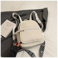 Detail of cream canvas backpack with geometric patterned straps on minimalist bedding - White