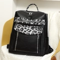 Close-up of a leopard print backpack with multiple zippers and black leather textures - Black