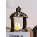 Vintage house-shaped LED candle lamp in black-gold finish on a white book surface - Bronze