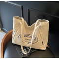 Detalle de bolso tote de lona beige con logo azul y correa resistente sobre silla de cuero - Beige