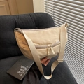 Beige crescent canvas crossbody bag with adjustable wide strap on grey corduroy sofa - Off-white