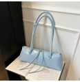 Close-up of light blue patent leather baguette bag with dual straps on an open book - Blue