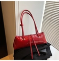 Close-up of bright red patent leather baguette bag with dual straps and silver eyelets - Red