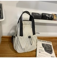 Close-up of off-white nylon backpack with black drawstring toggles and multi-pocket detail - White