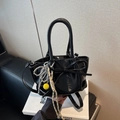 Borsa a secchiello nera lucida a pieghe con fiocco e ciondoli poggiata su libro bianco - Con Ciondolo / Nero