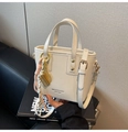 Close-up of a cream textured mini bucket bag with gold charms on a book background - With Pendant / Off White