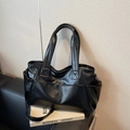 Large black faux leather tote bag with side pockets and crossbody strap on sofa - Black