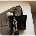Detail of a black glossy leather tote bag with a colorful braided rope pendant accessory - Black