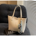 Detail of cream white leather tote bag with cute dog charm on a plush sofa - White