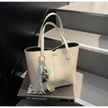 Detail of cream leather tote bag featuring plush bear charm and decorative cords on straps - Gray