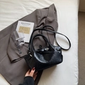 Bolso cubo negro brillante con hebilla y correa ajustable sobre una chaqueta gris - Negro sin Colgante